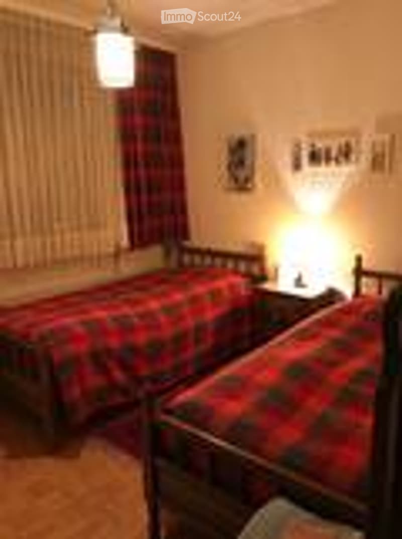 Cozy bedroom with two single beds, each with a plaid blanket, nightstands, and bedside lamps.