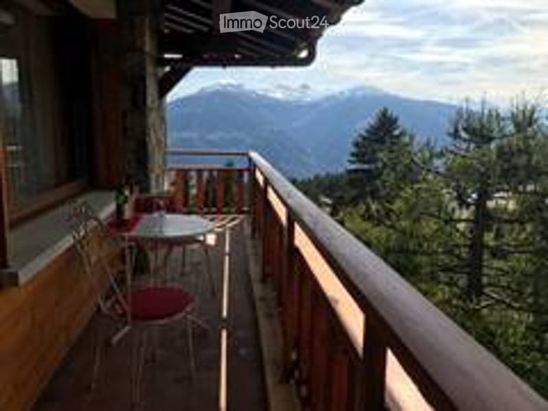 Balcony with wooden railing, outdoor furniture including a table and chairs, scenic mountain view in the background.
