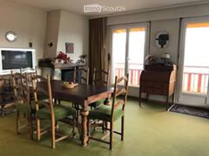 Dining room with a wooden dining table and chairs, a television, and a cabinet, with large windows and a balcony view.