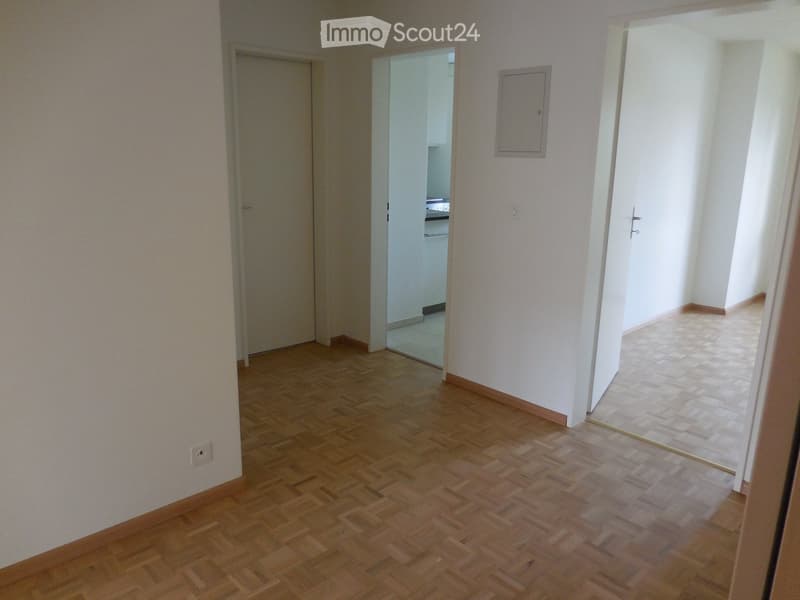 Empty hallway with wooden flooring, white walls, and doors leading to other rooms.