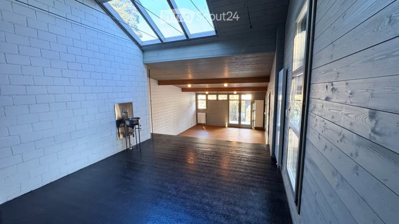 Modern hallway with white brick walls, dark grey floor, skylight ceiling, and a small sink area on the left.