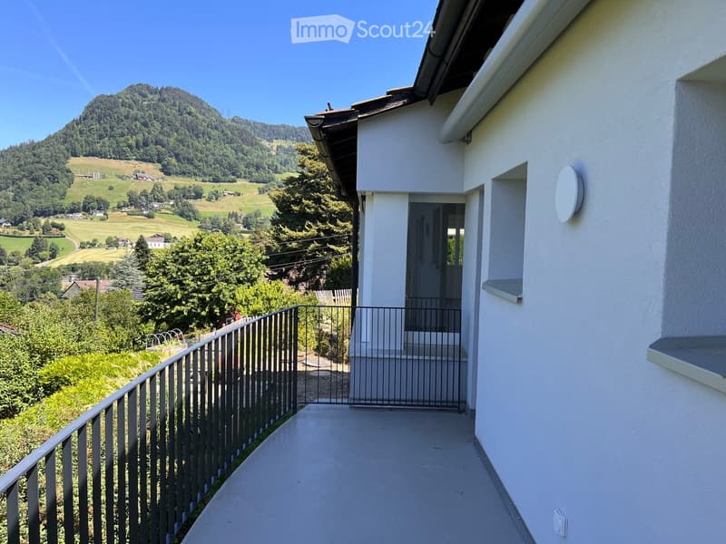 Balcony with metal railing, overlooking a green landscape and distant hills.