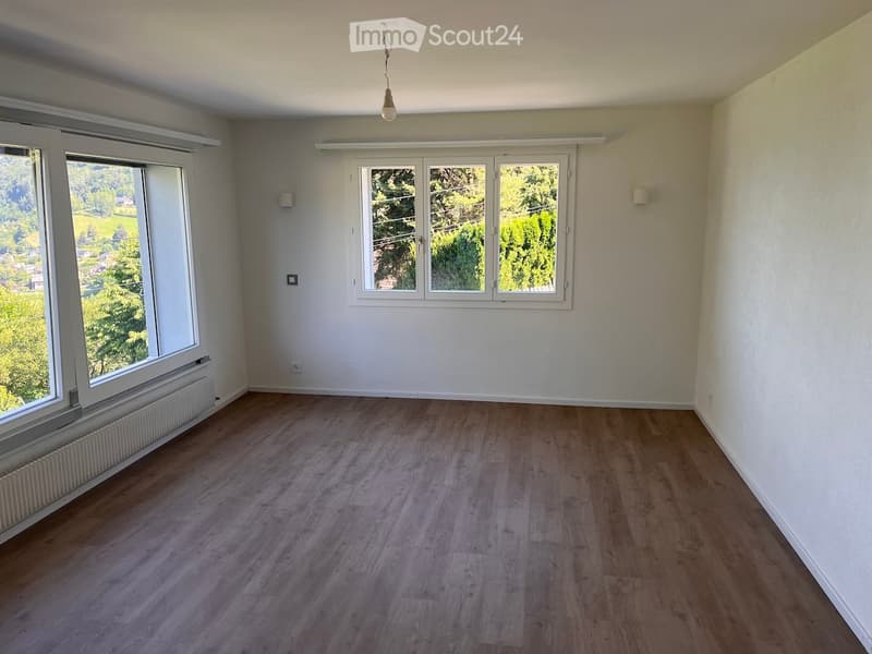 Empty room with wooden flooring, white walls, large windows, and a radiator. No furniture or equipment present.