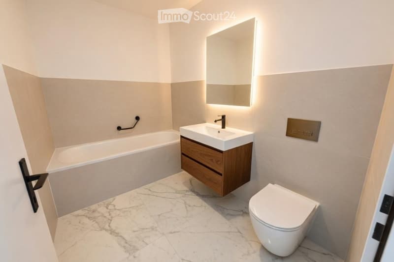 Modern bathroom with a white bathtub, a wooden sink cabinet, a toilet, and a large illuminated mirror above the sink. The floor is covered with marble tiles.