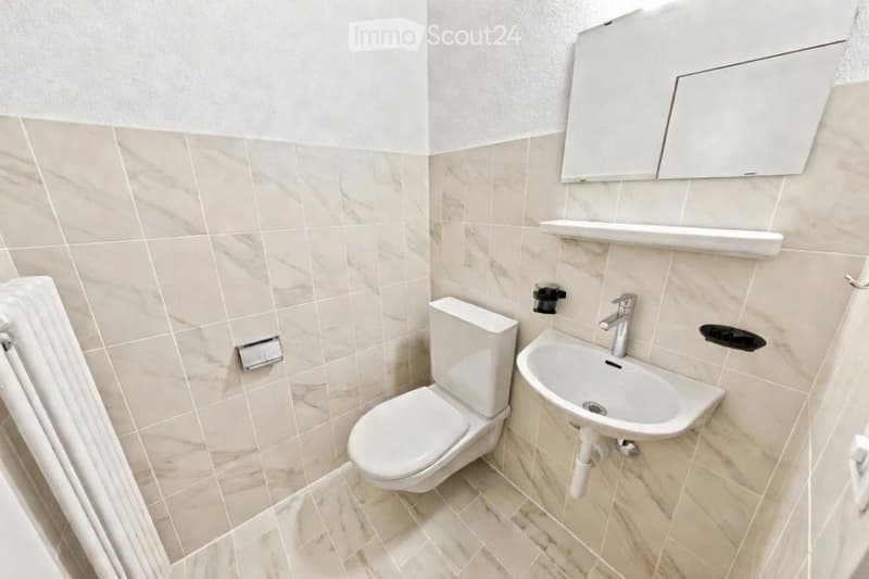 Modern bathroom with beige marble tiles, white toilet, sink, and mirrored cabinet.