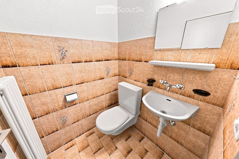 Bathroom with beige tiled walls and floor, white toilet, sink, mirror, and faucet.