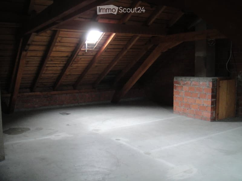 Empty attic space with wooden beams, concrete floor, and a small skylight window letting in natural light.
