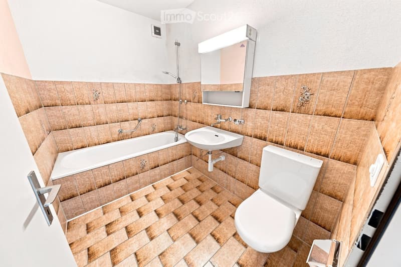 Bathroom with wooden tiled walls and floor, featuring a bathtub, sink, toilet, and a mirror with built-in storage.