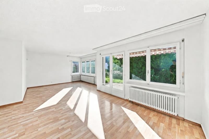 Empty room with wooden flooring, white walls, large windows, and radiators. No furniture or equipment present.