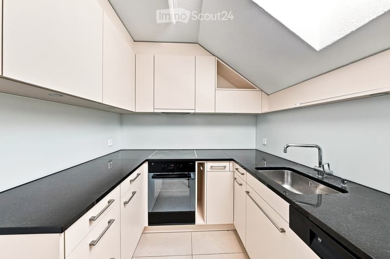 Modern kitchen with white cabinets, black countertops, stainless steel sink, and built-in oven.