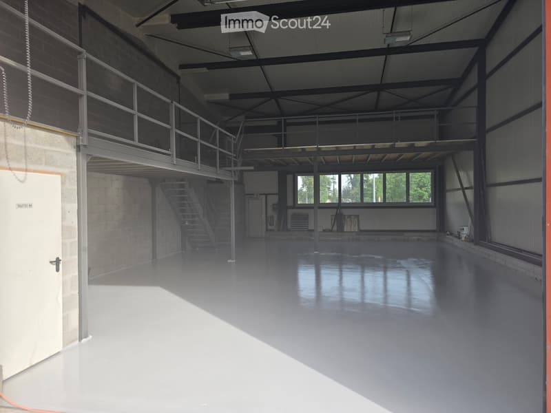 Large, empty industrial-style room with a polished concrete floor, metal staircase leading to an upper level, and large windows allowing natural light to enter.