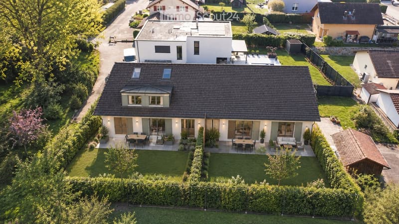 Aerial view of a modern two-story house with a well-maintained garden, patio seating areas, and surrounding greenery.