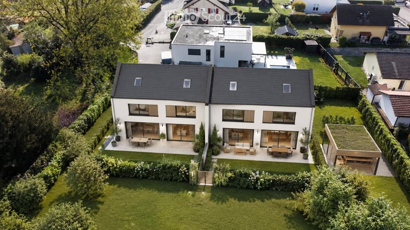 Modern two-story house with a flat roof, large windows, and a spacious garden with outdoor seating areas.