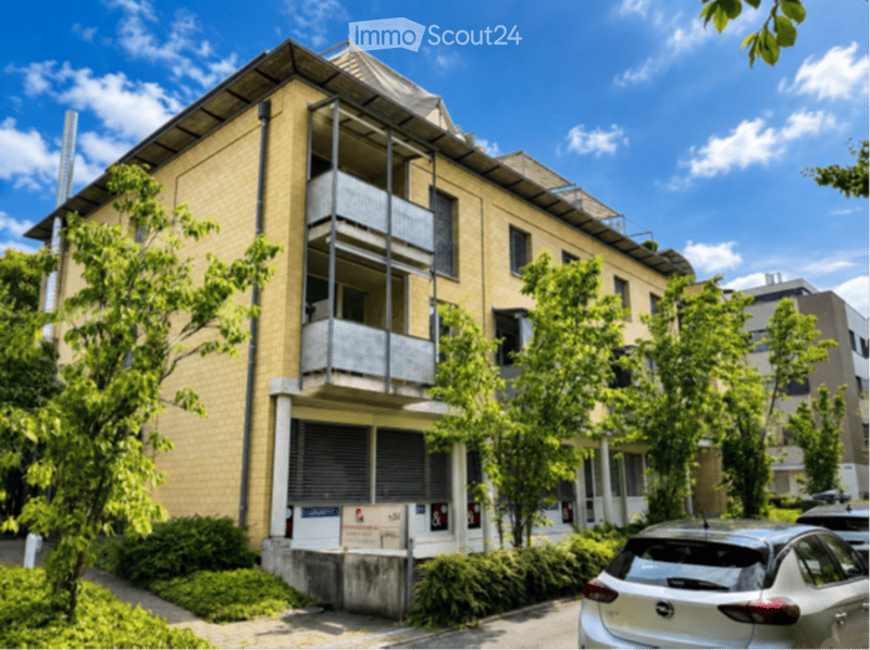 Multi-story residential building with yellow brick facade, multiple balconies, and surrounding greenery.