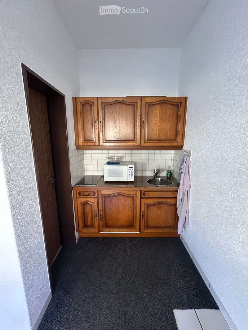 Compact kitchen with wooden cabinets, microwave, sink, and countertop.