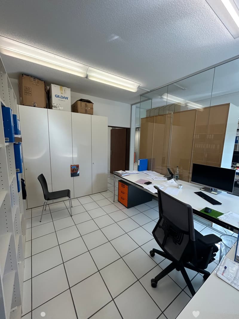 Office space with white tiled floor, desk with computer setup, chairs, filing cabinet, and storage boxes.