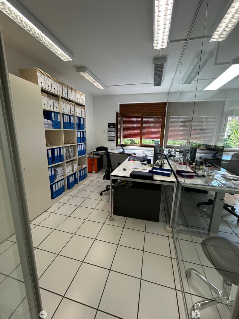 Office space with tiled floor, large windows, office desks, chairs, computers, and filing cabinets.