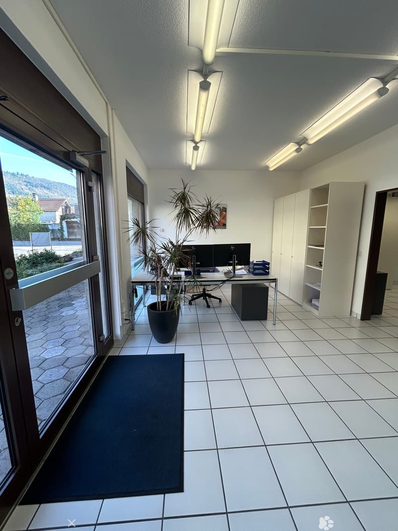 Office space with white tiled floor, large window, desk with computer, chair, potted plant, and white cabinets.