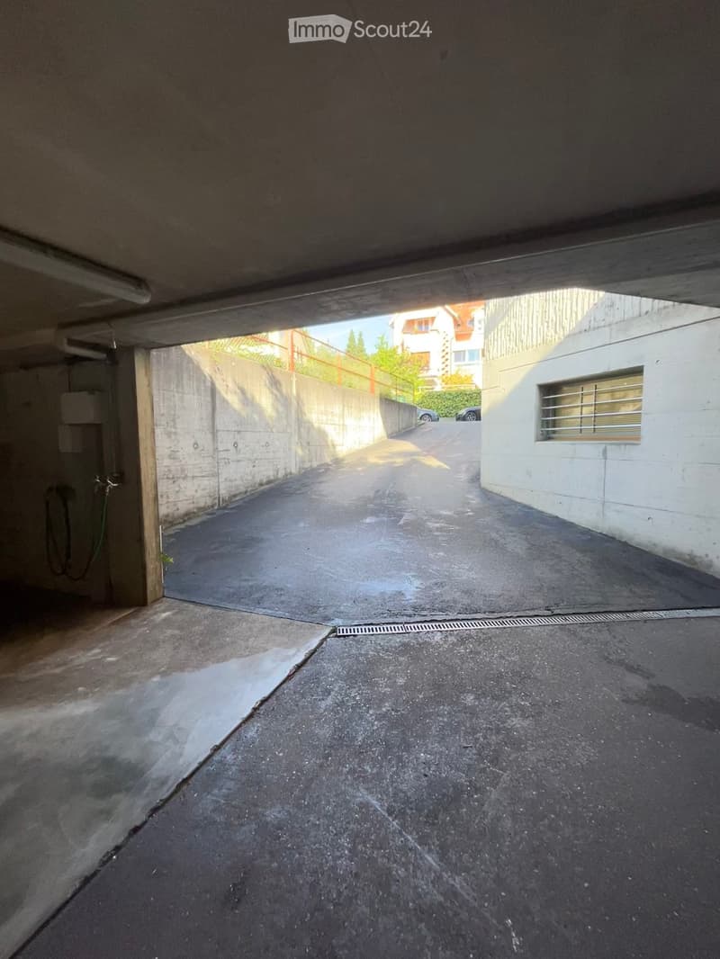 Underground parking area with concrete walls and floor, visible drainage grate, and a small window with metal bars on one side.