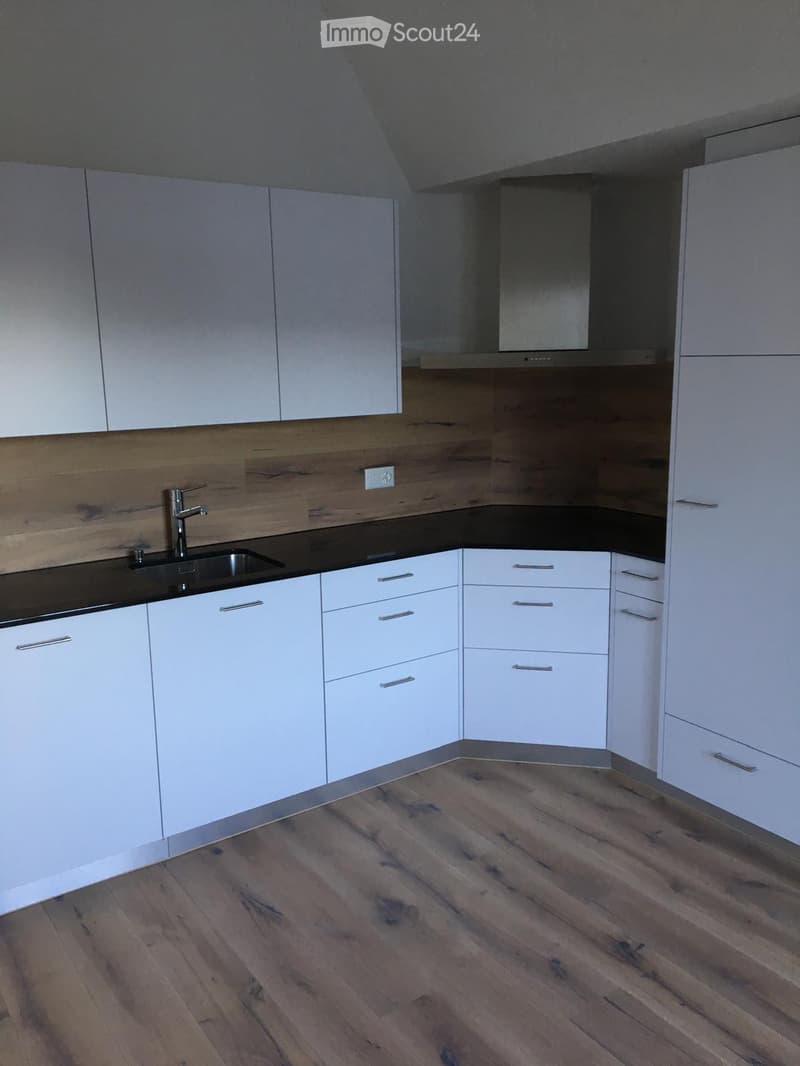 Modern kitchen with white cabinets, wooden accents, and a black countertop. Features a stainless steel sink and faucet.