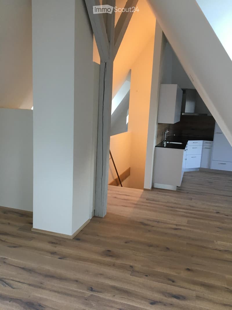 Spacious room with wooden flooring, white walls, and a small kitchen area featuring a sink, faucet, and cabinets.