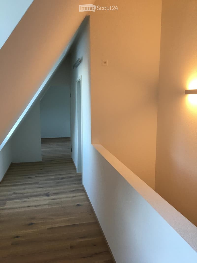 Empty hallway with wooden flooring, white walls, and a built-in light fixture on the right side. A door is visible at the end of the hallway.