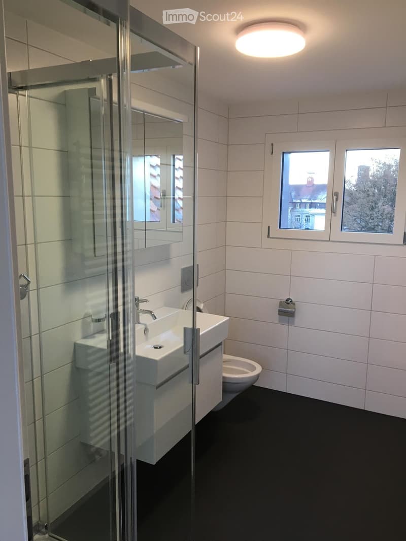 Modern bathroom with white tiles, black floor, sink, toilet, and a glass-enclosed shower stall.
