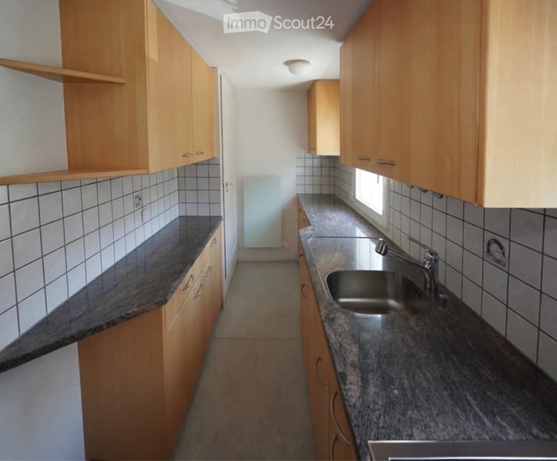 Modern kitchen with light wooden cabinets, granite countertops, and a stainless steel sink.