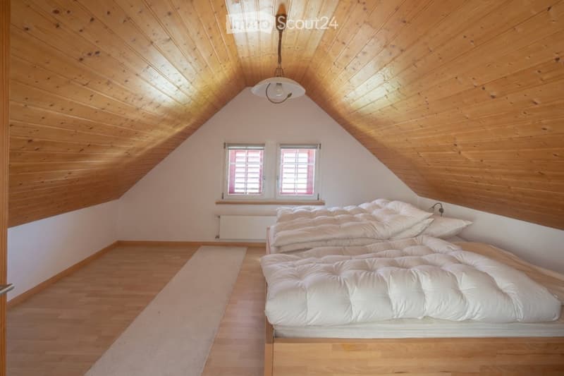 Cozy attic bedroom with wooden walls and ceiling, featuring a large bed with white bedding, a radiator, and a small rug on the floor.