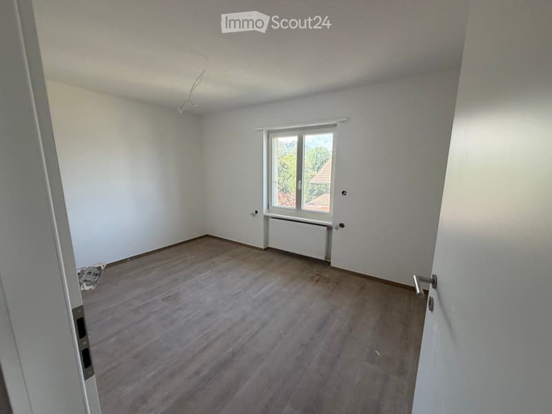 Empty room with wooden flooring, white walls, and a window with a radiator below it. No furniture or personal items are present.