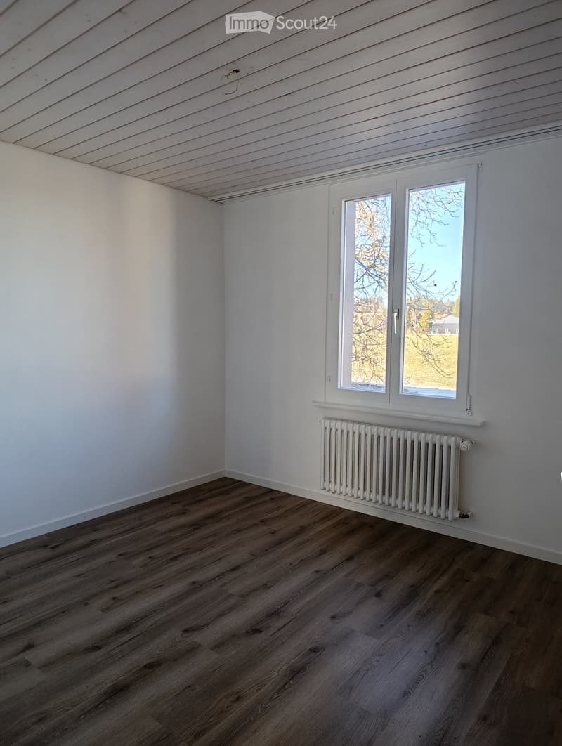 empty room with white walls, wooden floor, window, white radiator