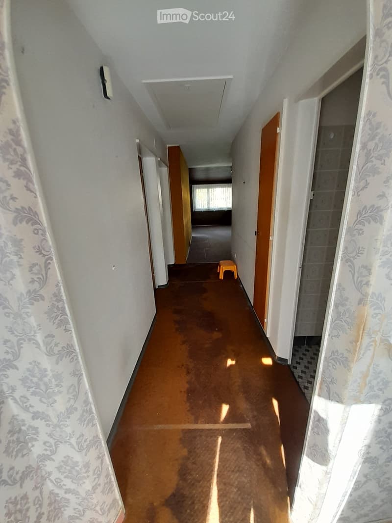 long hallway, white walls, brown floor, doors on both sides, small orange stool