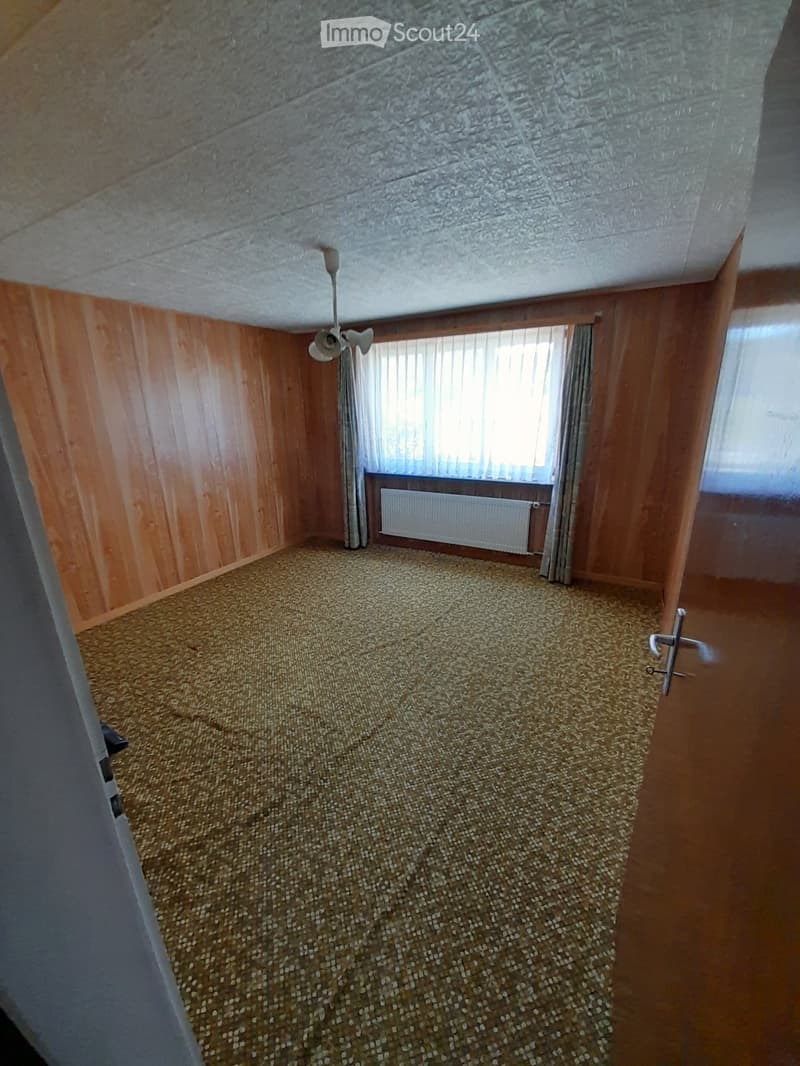 empty room, wooden walls, white ceiling, white radiator, window with curtains, carpeted floor
