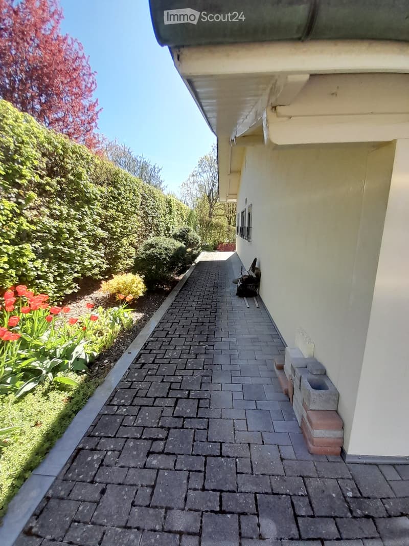 House exterior with a brick pathway, white walls, and a garden with flowers and bushes