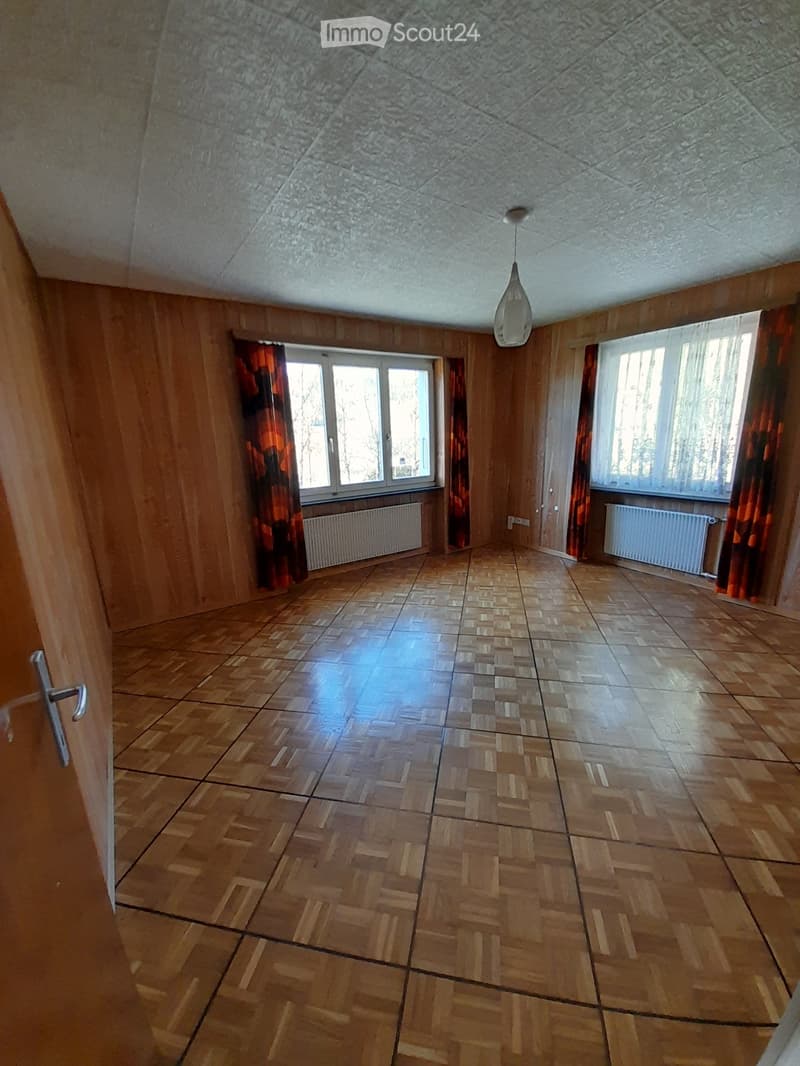 empty room, wooden floor, wooden walls, two windows, curtains, radiators, ceiling lamp