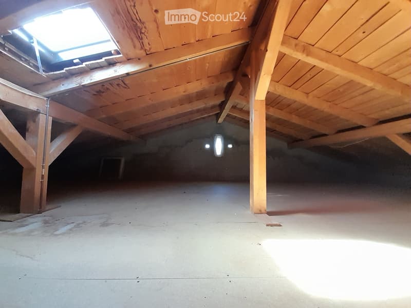 empty attic room with wooden beams, concrete floor, skylight