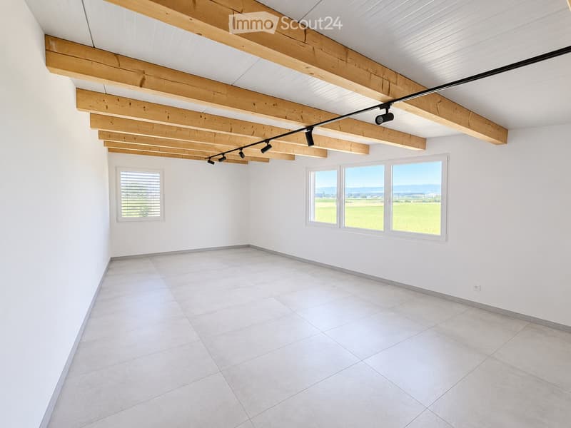 Empty room with white tiled flooring, white walls, large windows offering a scenic view, and exposed wooden beams on the ceiling.