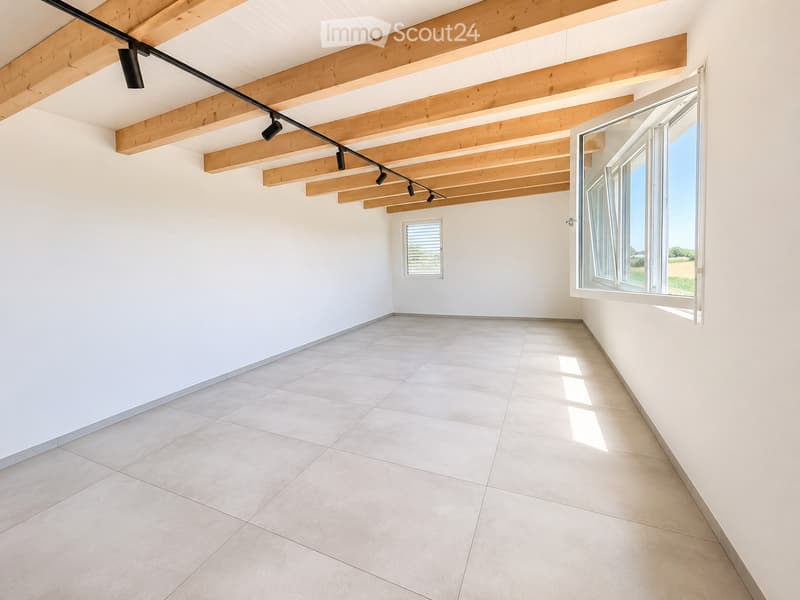 Empty room with white walls, tiled floor, large windows, and exposed wooden beams on the ceiling.