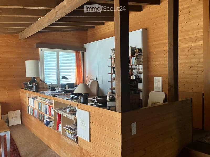 Cozy wooden-paneled room with a desk, chair, lamp, bookshelf, telephone, bowl, and picture frames.
