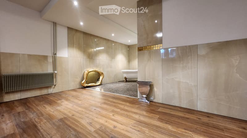 Modern bathroom with wooden flooring, large mirror, bathtub, radiator, and decorative golden mirror on the floor.