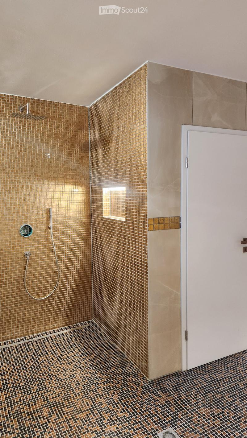 Modern bathroom with gold mosaic tiles on walls and floor, showerhead, and a small window.