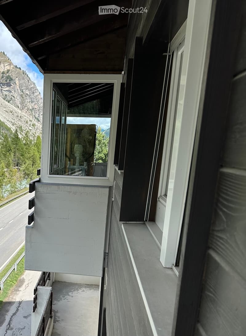 Balcony with white railings, overlooking a road and mountainous landscape with trees.