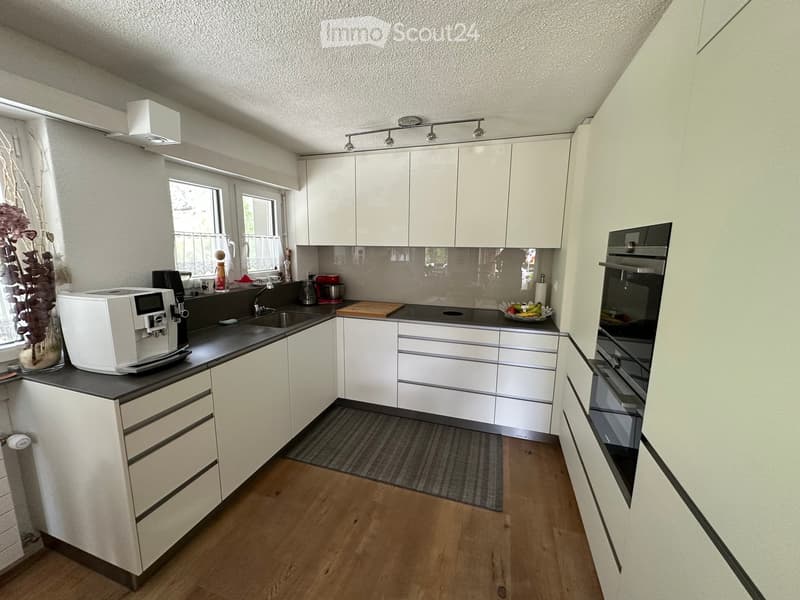 Modern kitchen with white cabinets, wooden flooring, and various appliances including a coffee machine, oven, and sink.