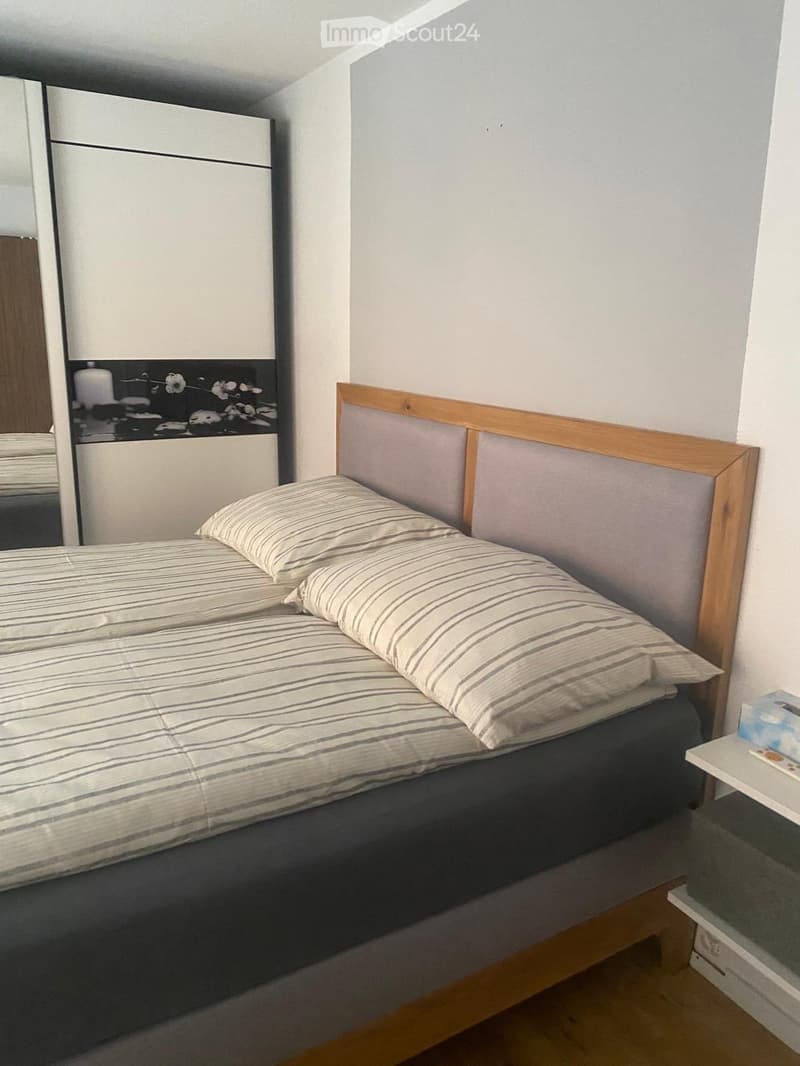 Cozy bedroom with a single bed, wooden headboard, striped bedding, and a small nightstand with a mirror.