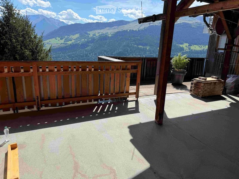 Balcony with wooden railing, overlooking a scenic mountain landscape, with a potted plant and wooden crate.