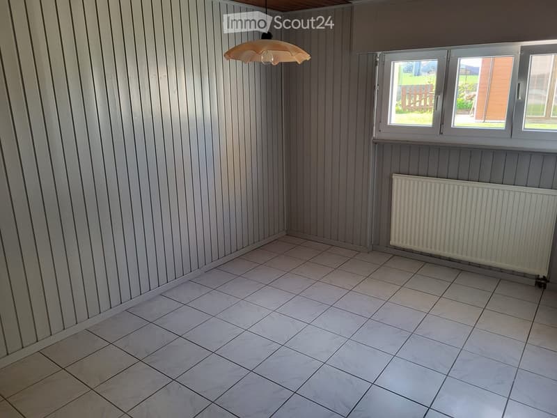 Empty room with tiled floor, paneled walls, radiator, and windows showing outdoor view.
