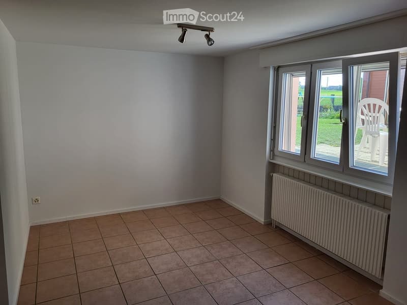Empty room with tiled floor, white walls, large windows, radiator, and track lighting.