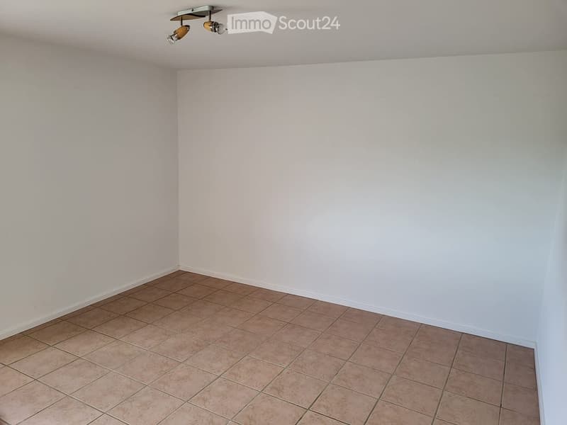 Empty room with beige tiled floor and white walls, featuring a ceiling light fixture.