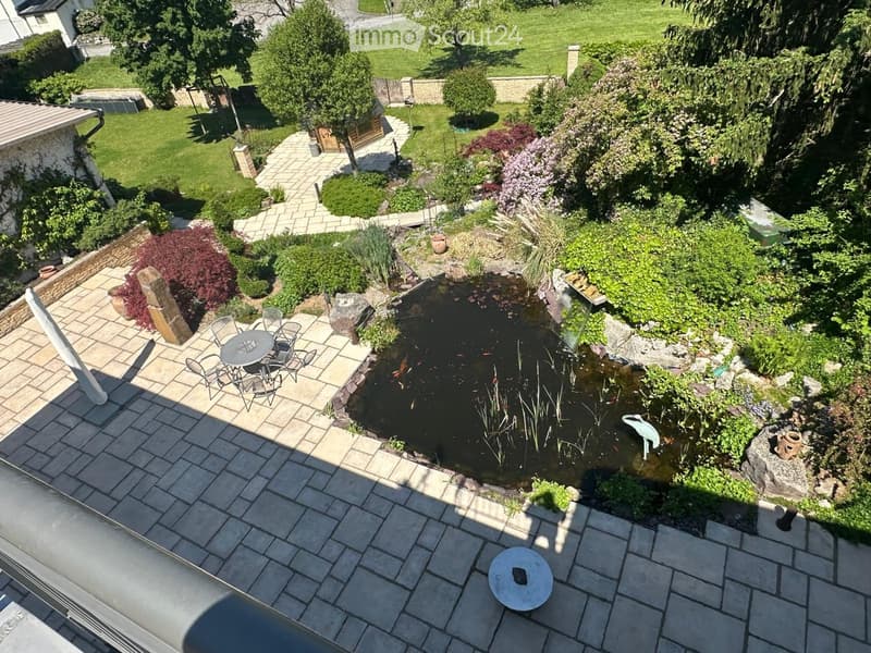 Well-maintained garden with a pond, seating area, and various plants and trees.