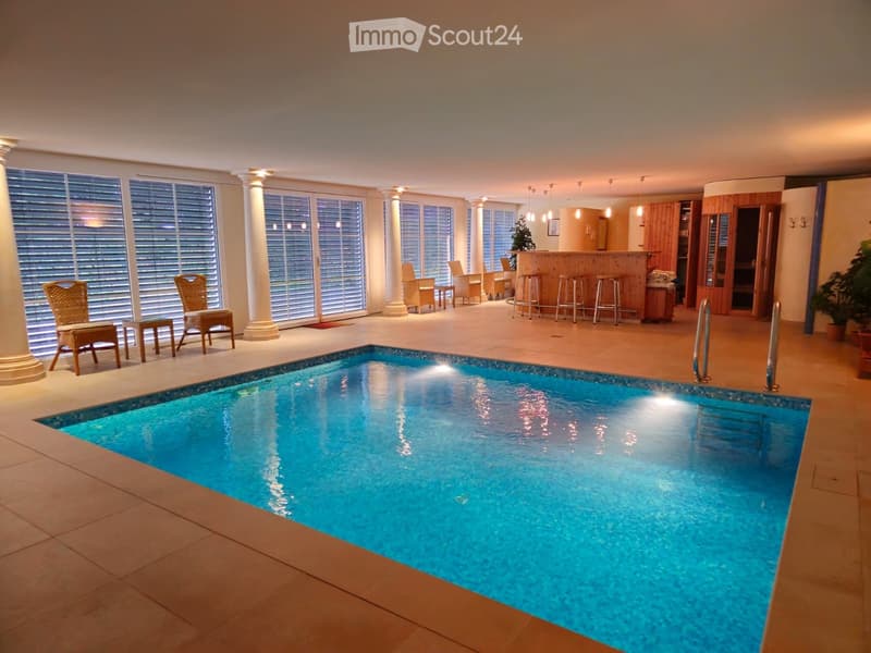 Indoor pool area with large windows, wicker chairs, small tables, and bar area with stools.
